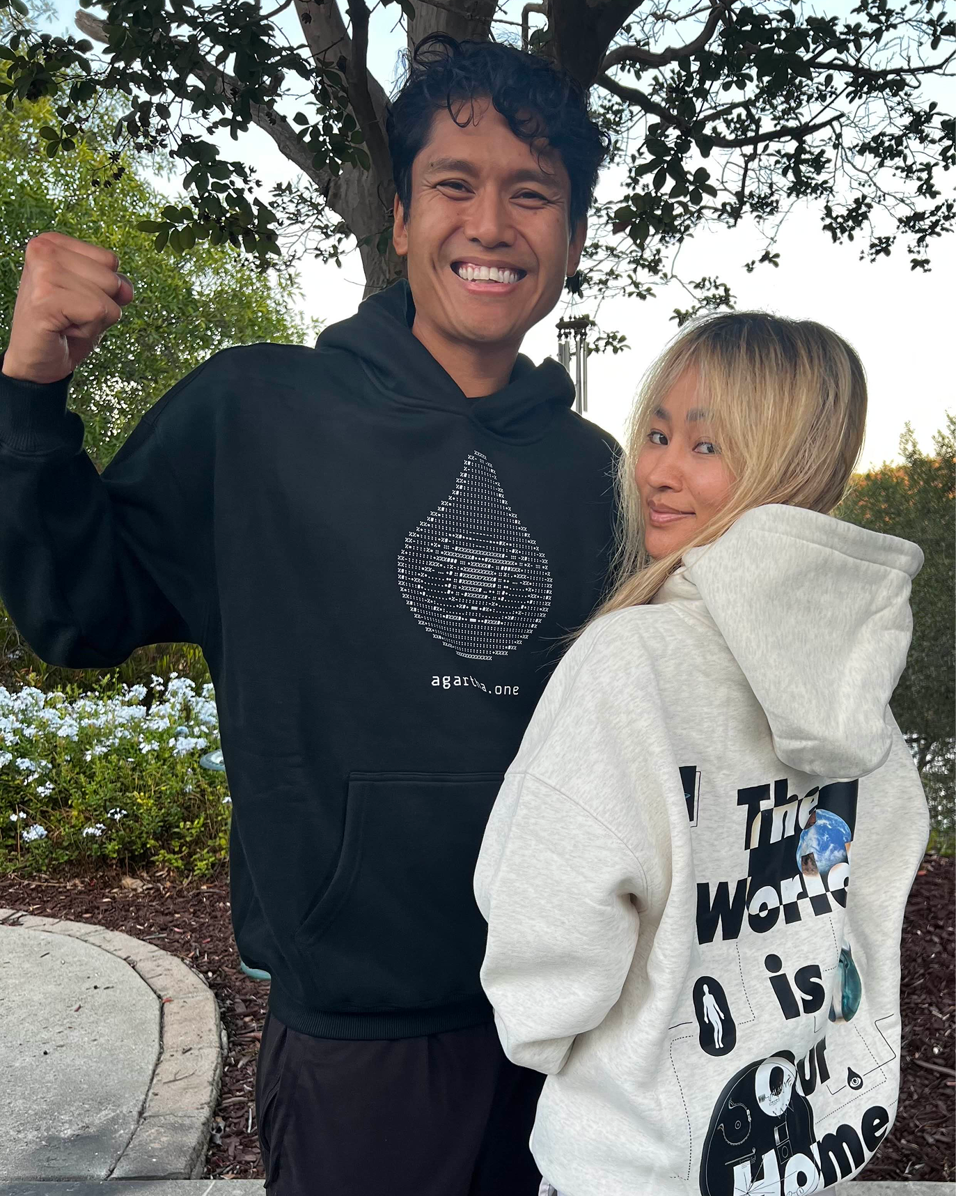 Two people wearing hoodies with visible text and graphics outdoors.